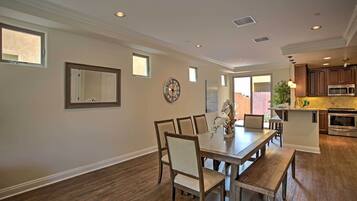 A dining area with a wooden table and chairs, a clock on the wall, and a kitchen in the background.