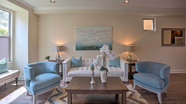 Un salon avec un canapé blanc, deux fauteuils bleus, une table basse en bois et un tableau accroché au mur.