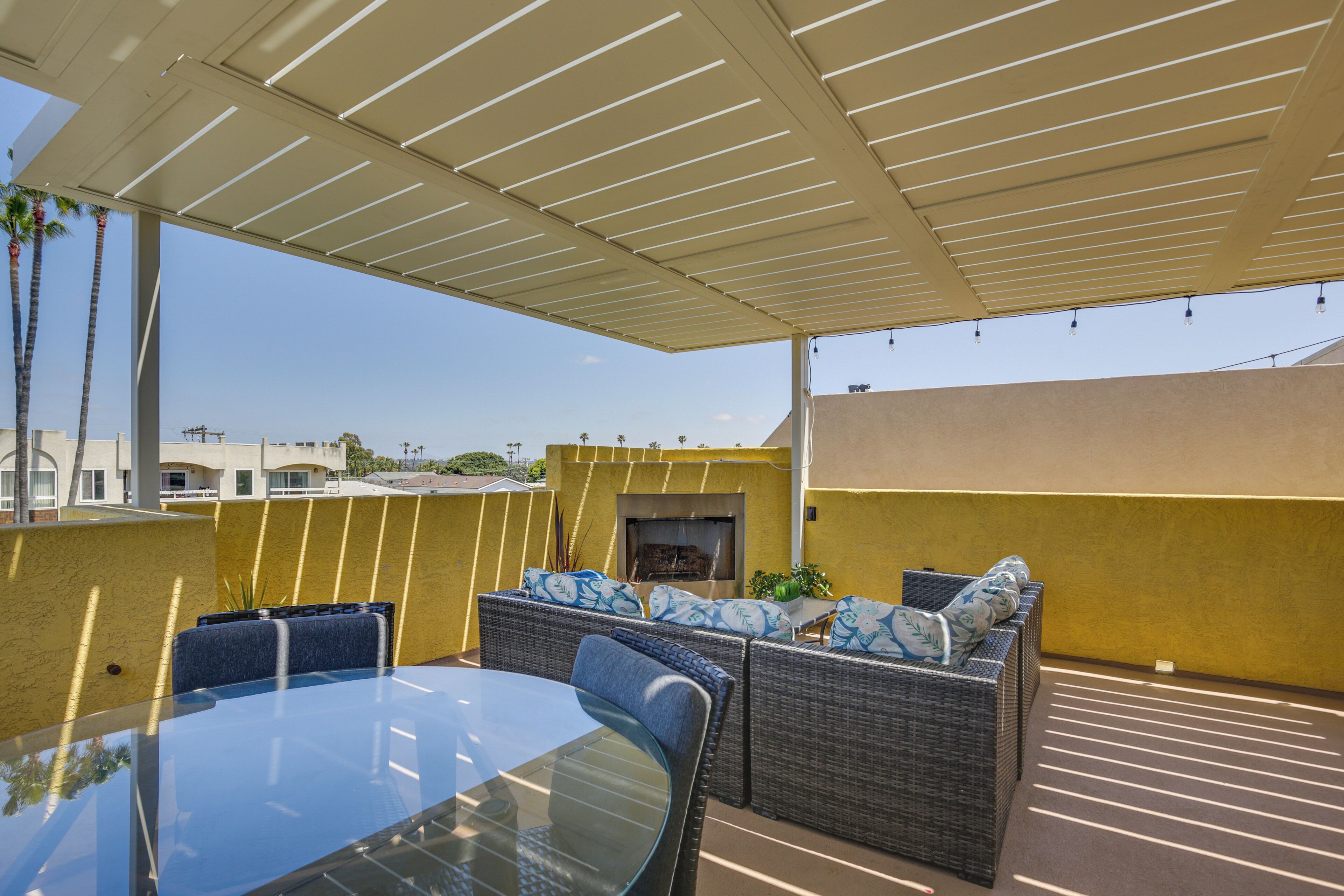Una veranda esterna coperta con tavolo in vetro e mobili in vimini, un braciere e vista sullo skyline della città.