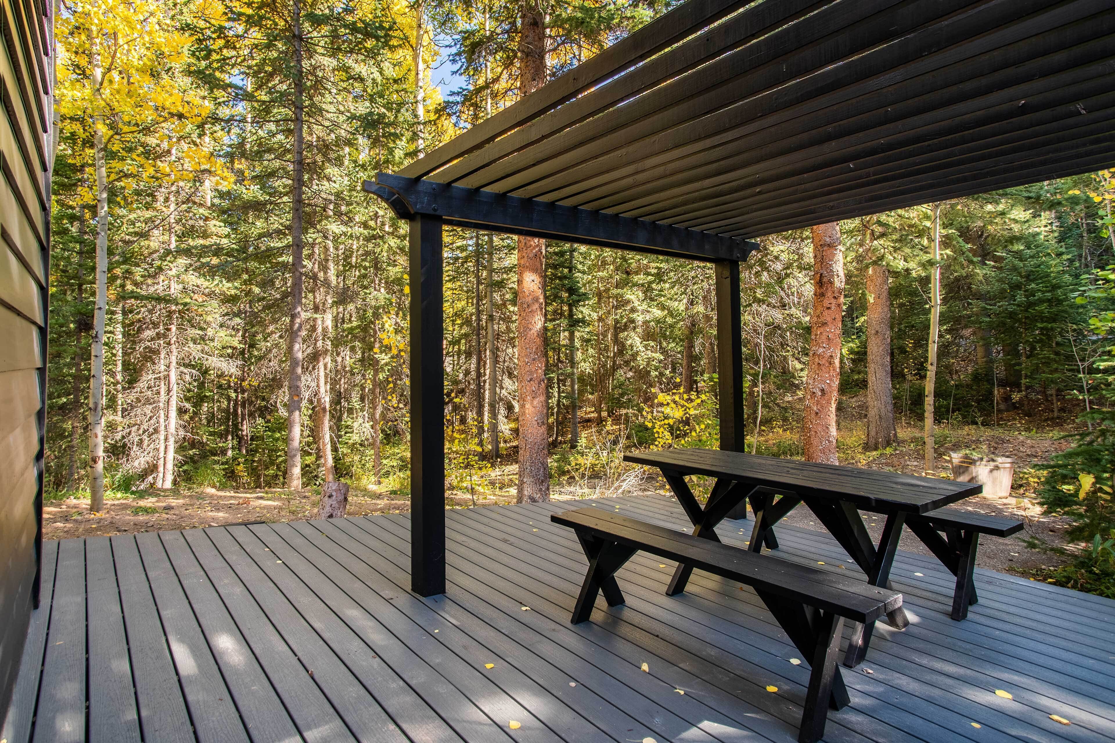 A wooden deck with picnic tables, surrounded by a forest.