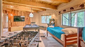 A cozy room with a foosball table, a bed, a TV, and large windows offering a view of the forest. - 'zen Forest Mountain Retreat' Tahoe Home W/hot Tub (South Lake Tahoe)