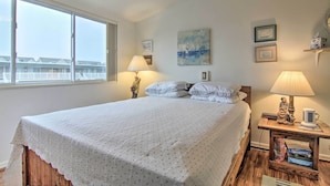 Een slaapkamer met een groot bed, een nachtkastje met een lamp, een klein beeldje en een schilderij aan de muur.
