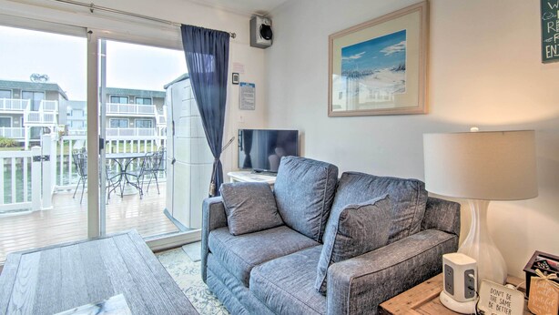 Een woonkamer met een grijze bank, een televisie, een lamp en uitzicht op een balkon met buitenmeubilair.