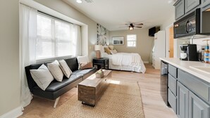 Un espacio habitable compacto con sofá, cama, zona de cocina y ventilador de techo.