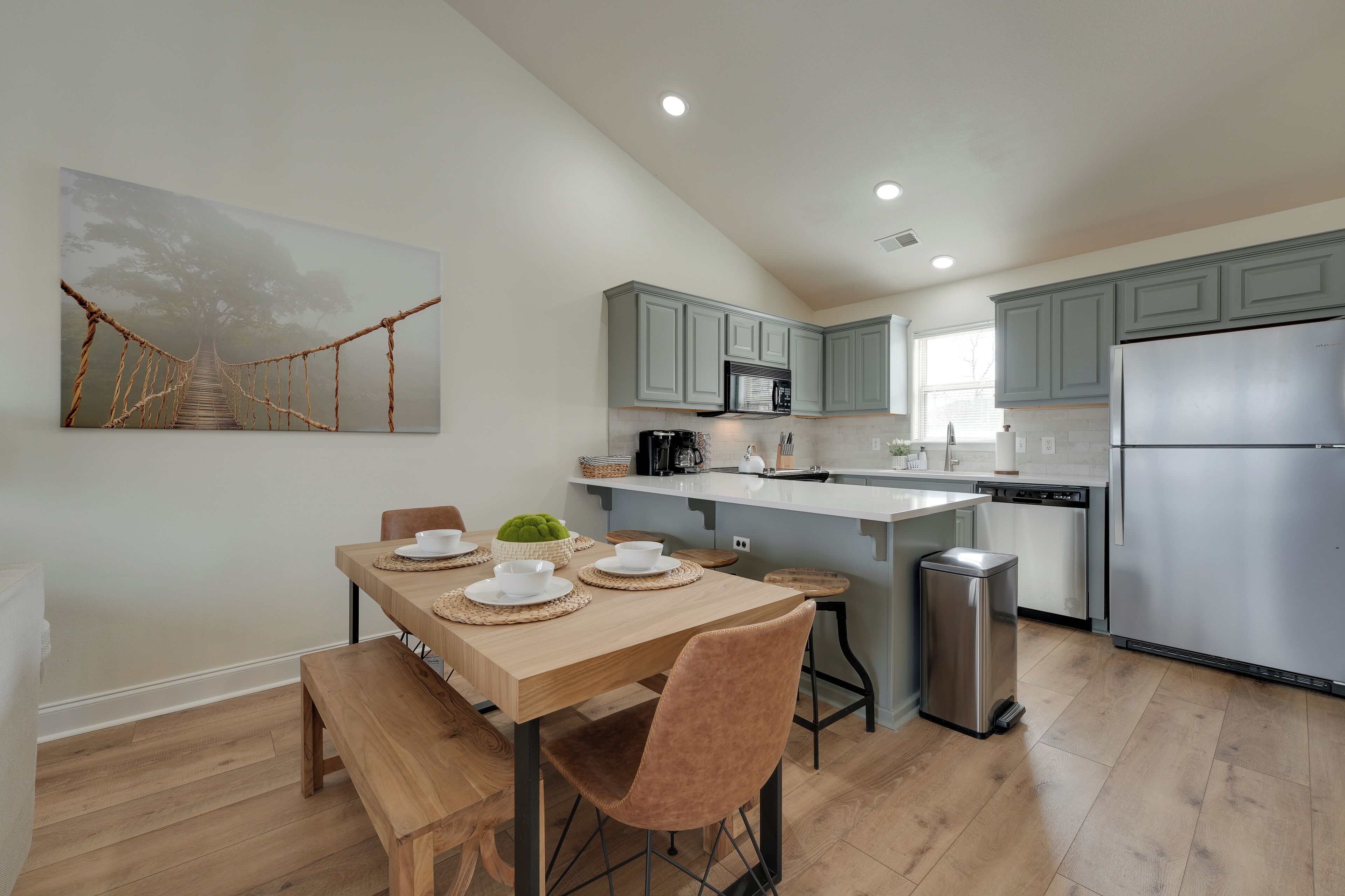 Una cocina moderna con armarios grises, electrodomésticos de acero inoxidable y una mesa de comedor de madera con sillas.