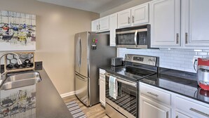 A modern kitchen with white cabinets, stainless steel appliances, a black countertop, and a tiled backsplash. - Middle Bass Condo w/ Balcony, Lake Erie Views (Put-in-Bay)