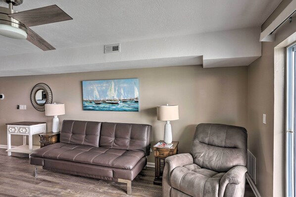 A living room with a sofa, a chair, a painting, a lamp, and a ceiling fan. - Middle Bass Condo w/ Balcony, Lake Erie Views (Put-in-Bay)