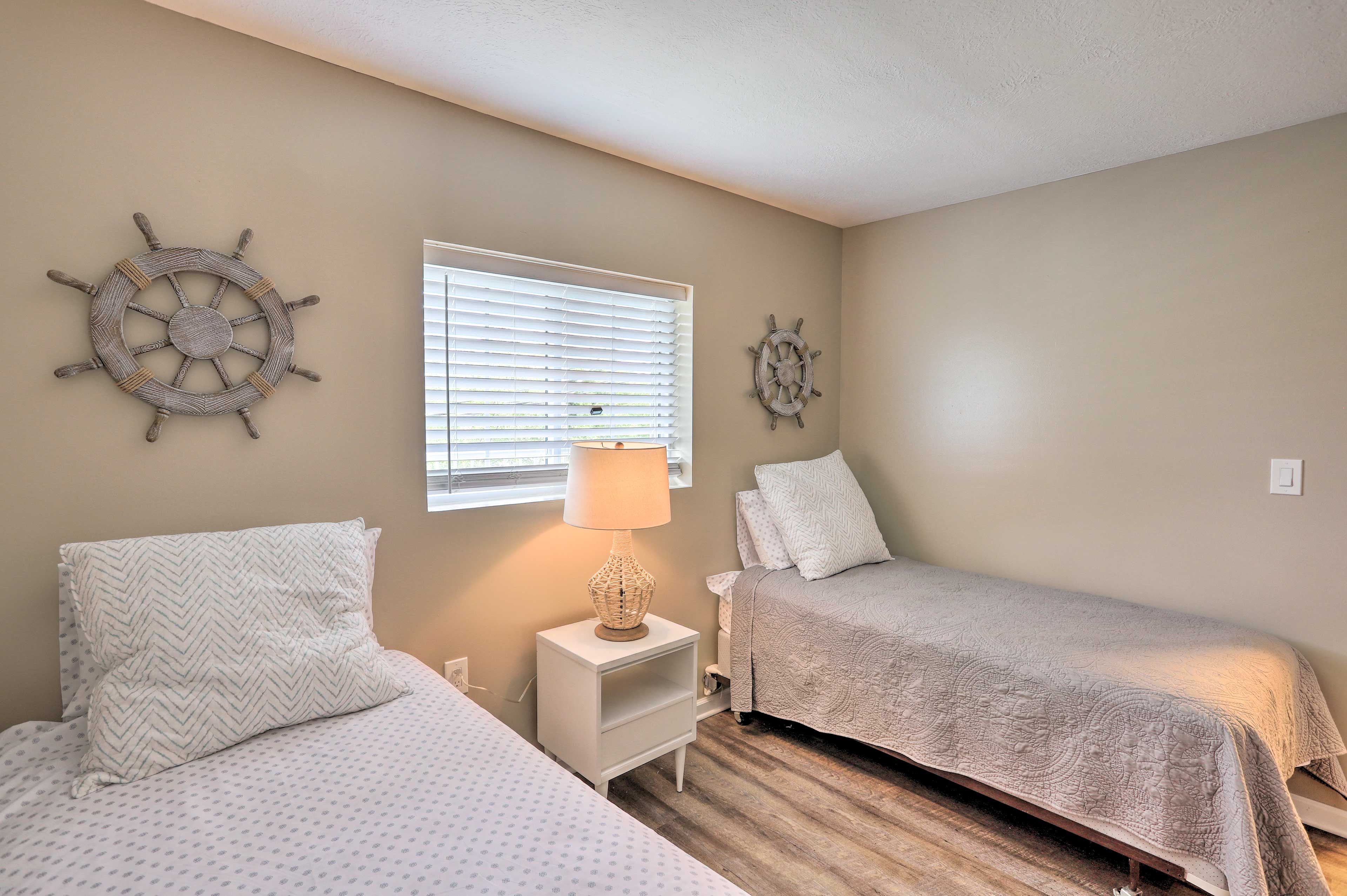A bedroom with two beds, a nightstand with a lamp, and two ship's wheel wall decorations.