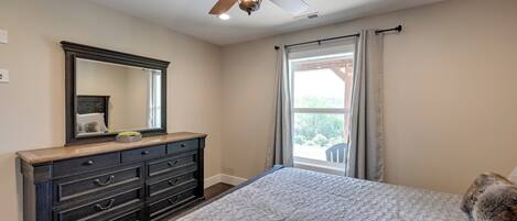 A bedroom with a large bed, a dark wooden dresser, a ceiling fan, and a window with curtains.