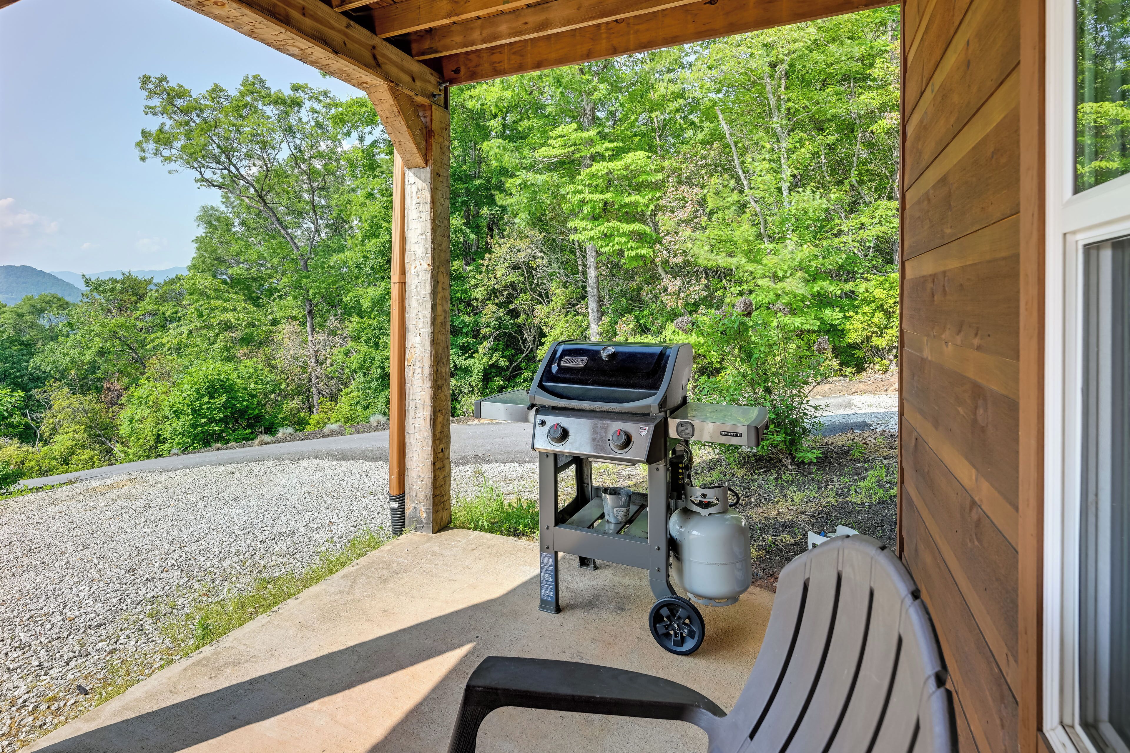 Un espacio al aire libre techado con una parrilla y una silla, rodeado de follaje y un sendero de grava.