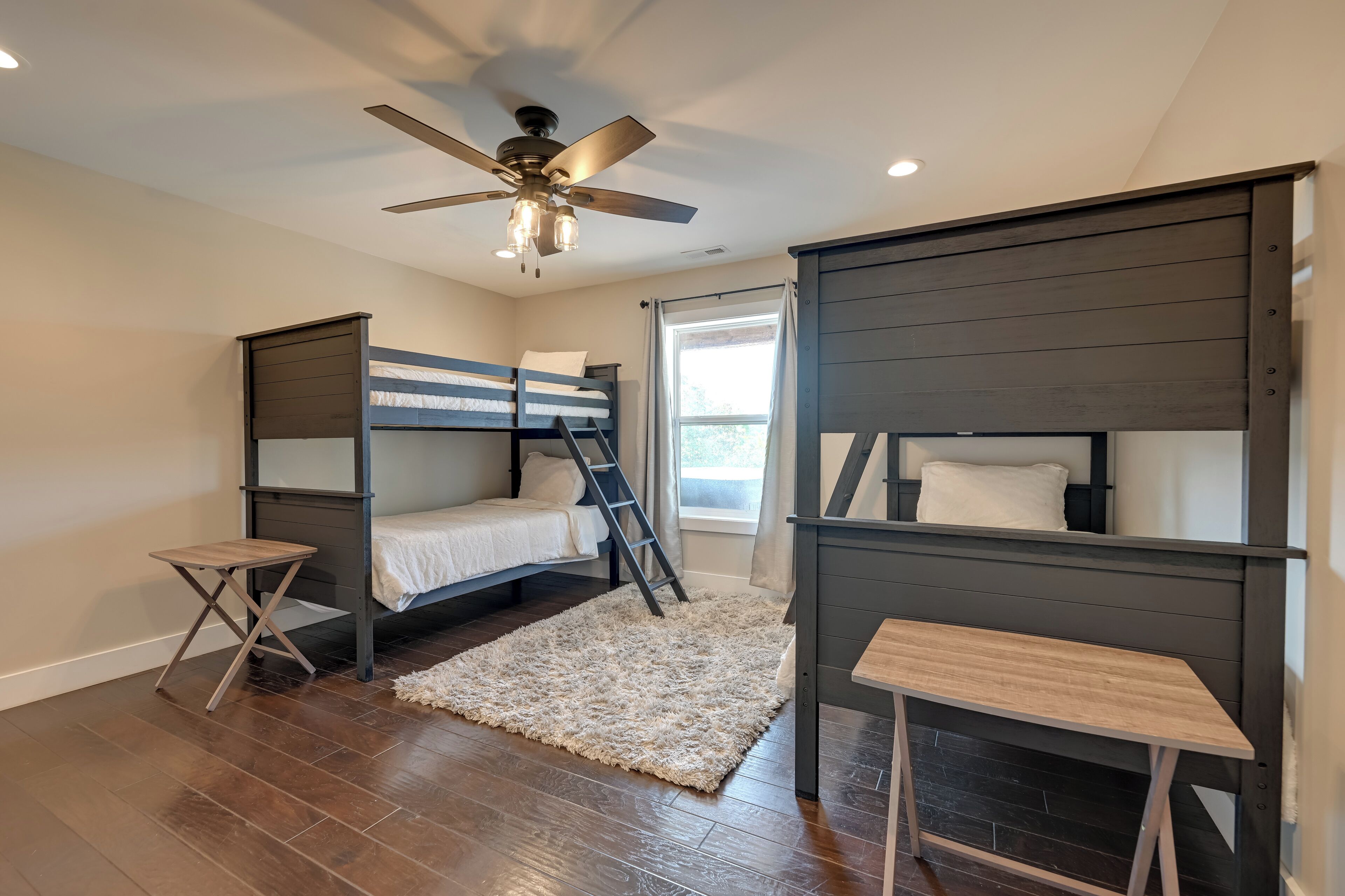 Une chambre avec deux lits superposés, un ventilateur de plafond, une petite table en bois et un tapis moelleux.