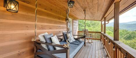 Terraza de madera con un sofá columpante, faroles y vista al bosque.