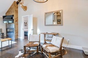 A modern living room with a fireplace, two leather chairs, a wooden table, and a mirror on the wall.
