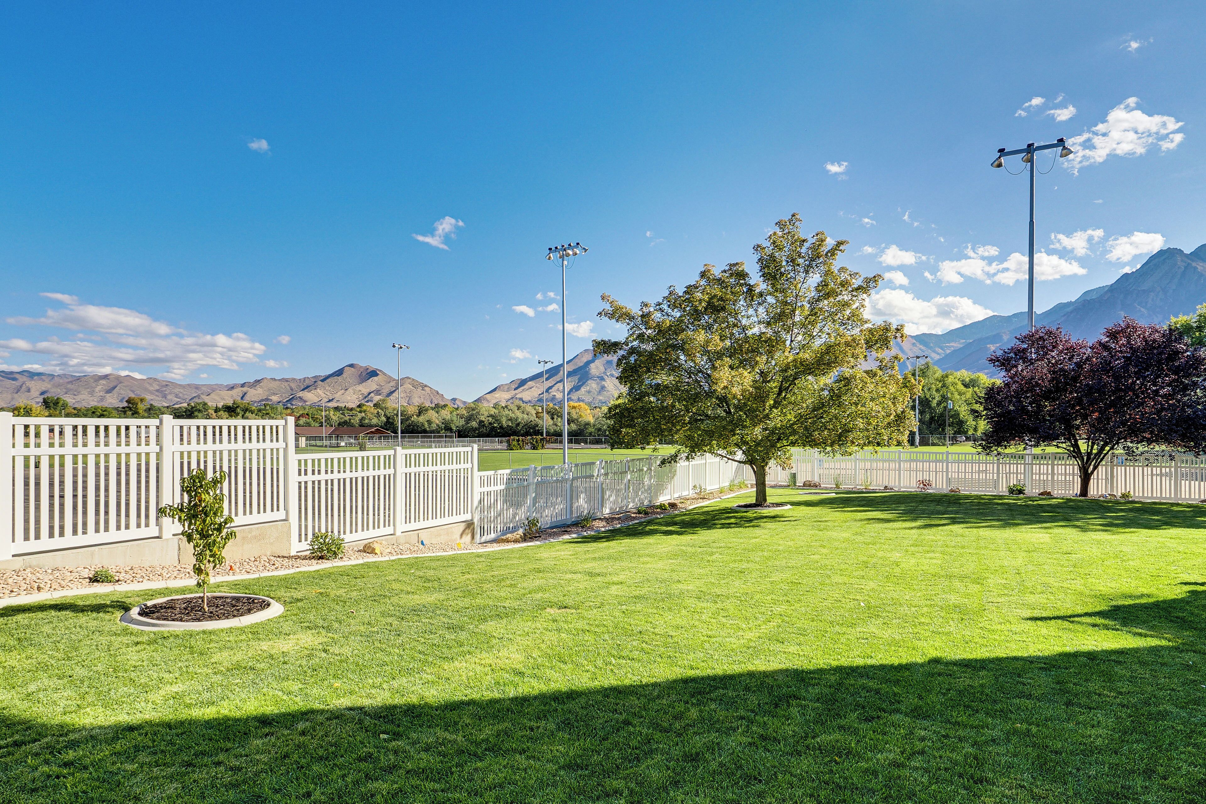 A well-maintained grassy area with a tree, a white fence, and a mountain range in the background.