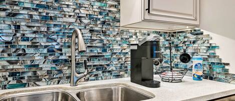 A kitchen with a marble backsplash, stainless steel sink, and a coffee maker.