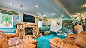 A living room with leather sofas, a stone fireplace, a television, and a mural of a shipwreck. - Mtn-view SLC Apt w/ Patio Near Downtown (Salt Lake City)