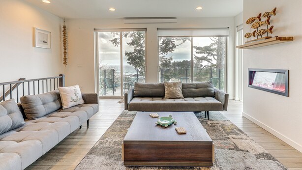 A modern living room with a sofa, coffee table, and a TV mounted on the wall. - Depoe Bay Townhome w/ Deck & Stunning Ocean Views! (Depoe Bay)