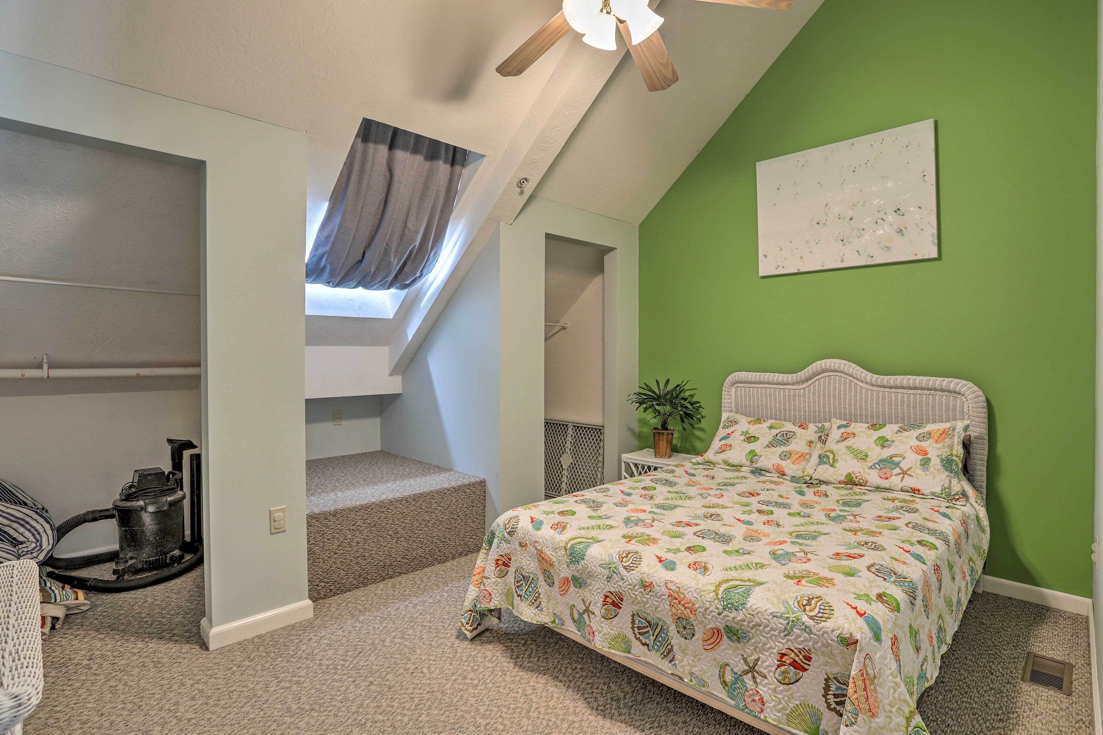 A bedroom with a bed, a window, a ceiling fan, and a green wall.