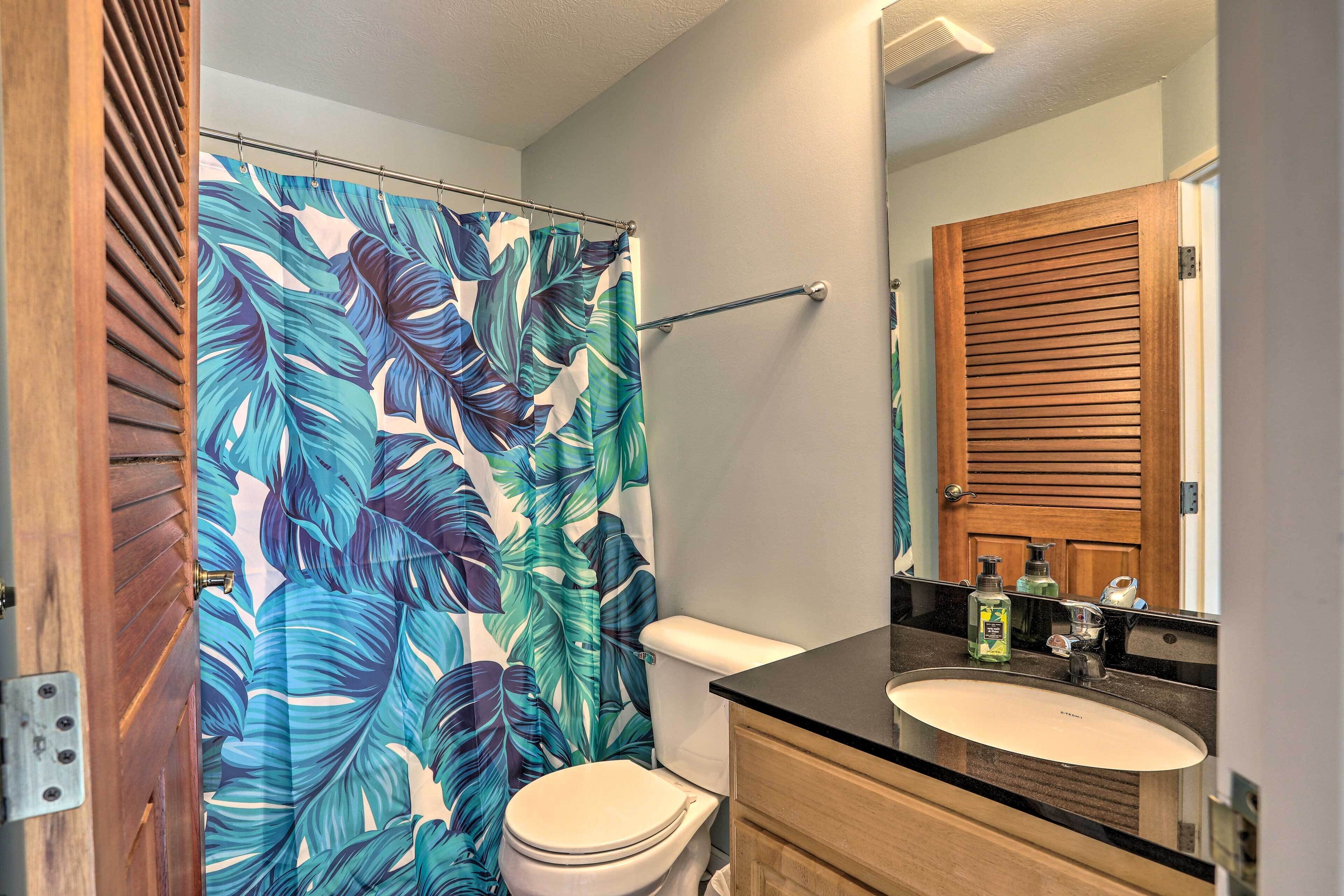 Un baño con inodoro, lavabo y cortina de ducha con estampado de hojas tropicales.