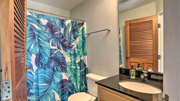 Un baño con inodoro, lavabo y cortina de ducha con estampado de hojas tropicales.