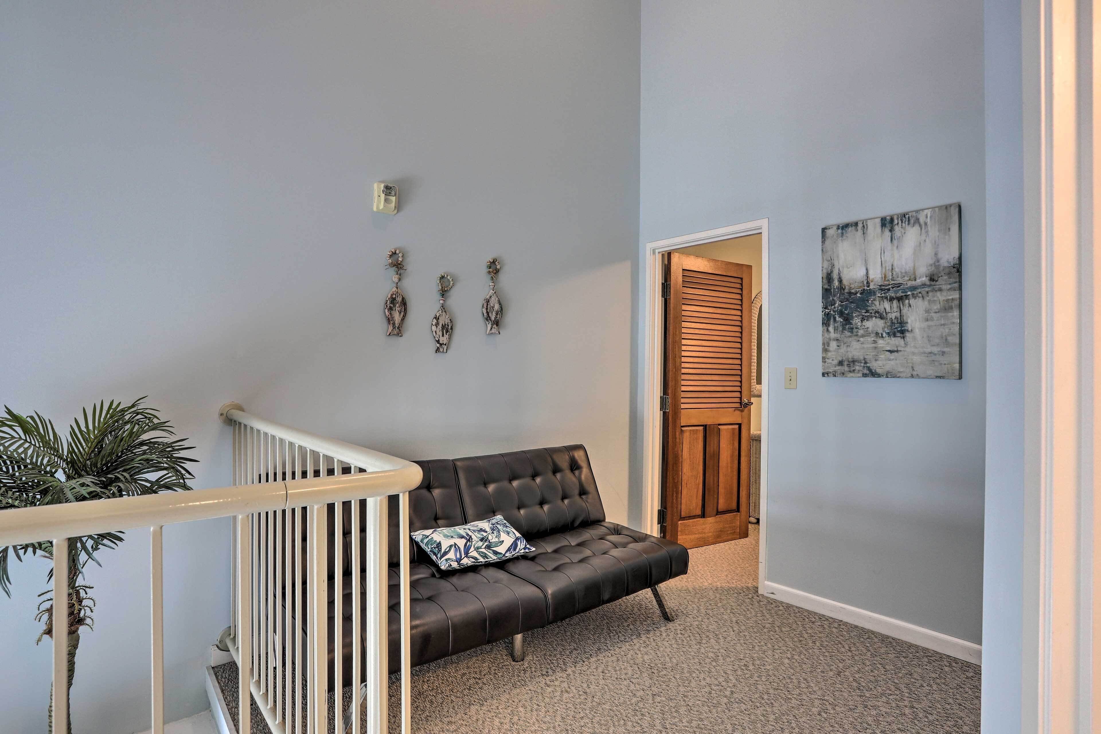A modern living room with a black leather sofa, a small plant, and a painting on the wall.