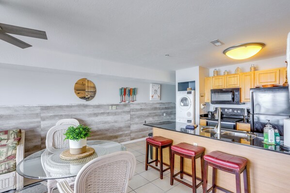 A modern kitchen with wooden cabinets, a stainless steel refrigerator, and a glass dining table with bar stools. - Cozy Lakefront Middle Bass Retreat w/ Balcony (Put-in-Bay)