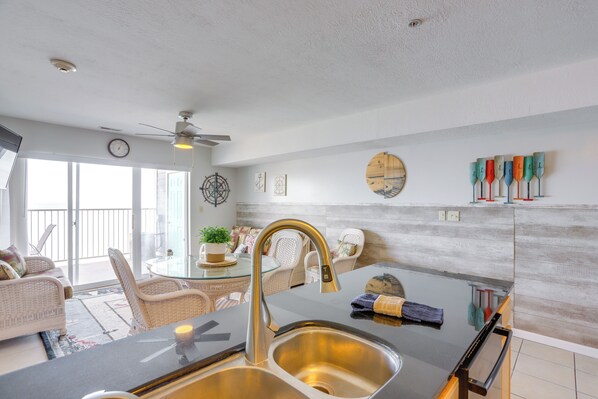 A modern kitchen with a stainless steel sink, a ceiling fan, and a dining area with wicker furniture. - Cozy Lakefront Middle Bass Retreat w/ Balcony (Put-in-Bay)