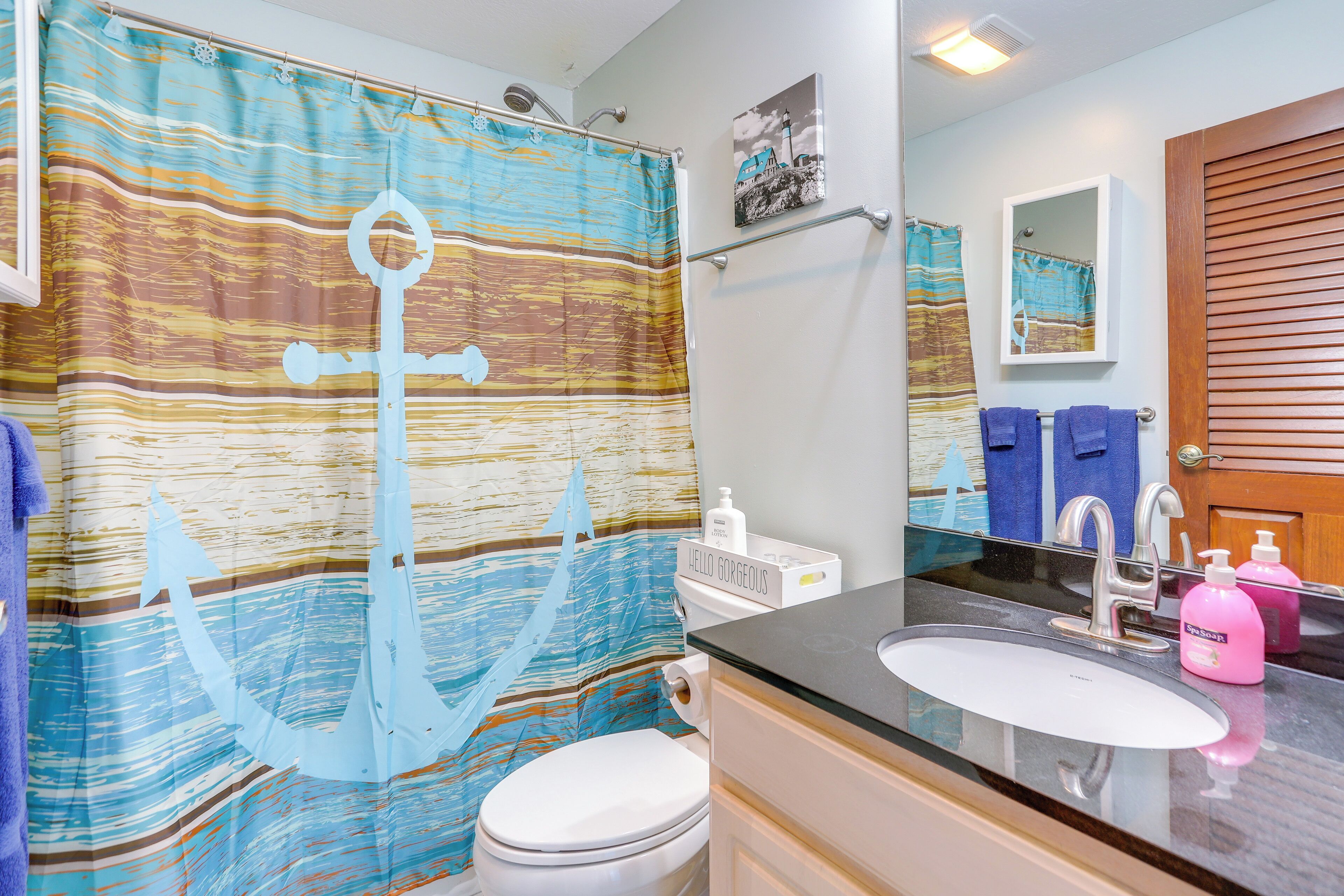 A bathroom with a striped shower curtain, a white toilet, a sink with a mirror, and a wooden door.