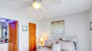Un dormitorio con cama, mesita de noche, ventilador de techo, puerta de madera y una pared con un cuadro.