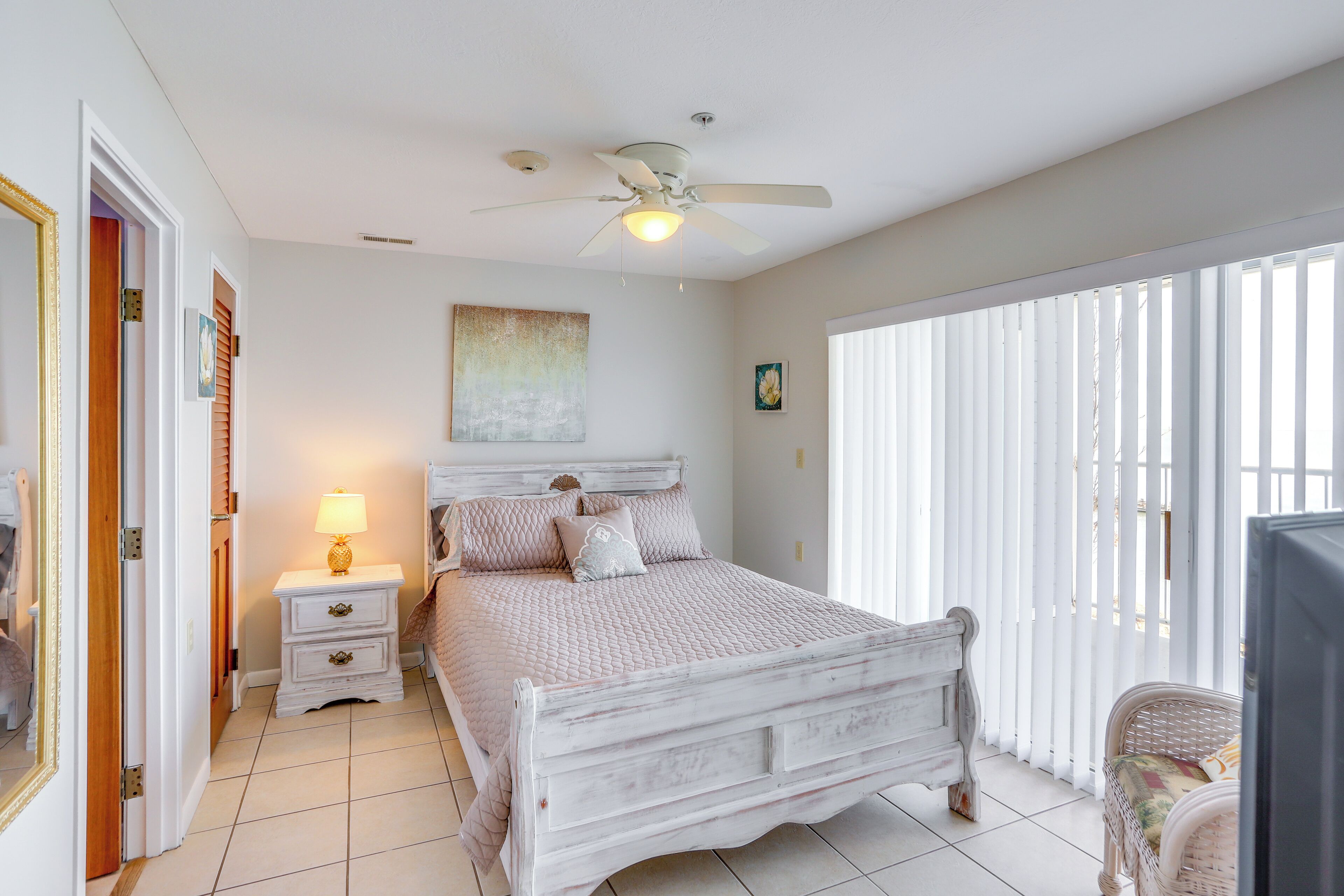 A bedroom with a bed, a nightstand, a ceiling fan, and a window with blinds.
