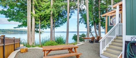A wooden picnic table and benches, a staircase leading to a building, and a view of a lake surrounded by tall trees.