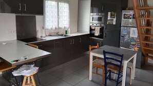 A modern kitchen with dark cabinets, a white countertop, a sink, and a dining area with a table and chairs. - Homestay (Chambéry)