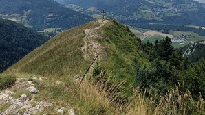 A mountain path with a cross, surrounded by green hills and a distant town. - Homestay (Chambéry)