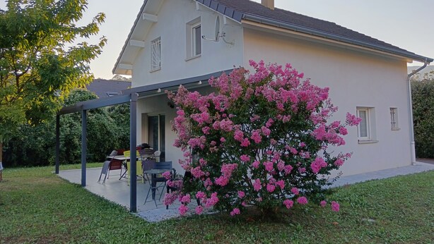 A two-story house with a covered patio area and a large flowering bush. - Homestay (Chambéry)