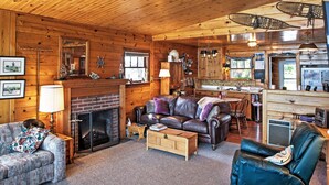 A cozy cabin interior with a fireplace, leather furniture, wooden walls, and a kitchen area. - Newport Cabin w/ Lakefront Private Porch & Grill! (Newport)