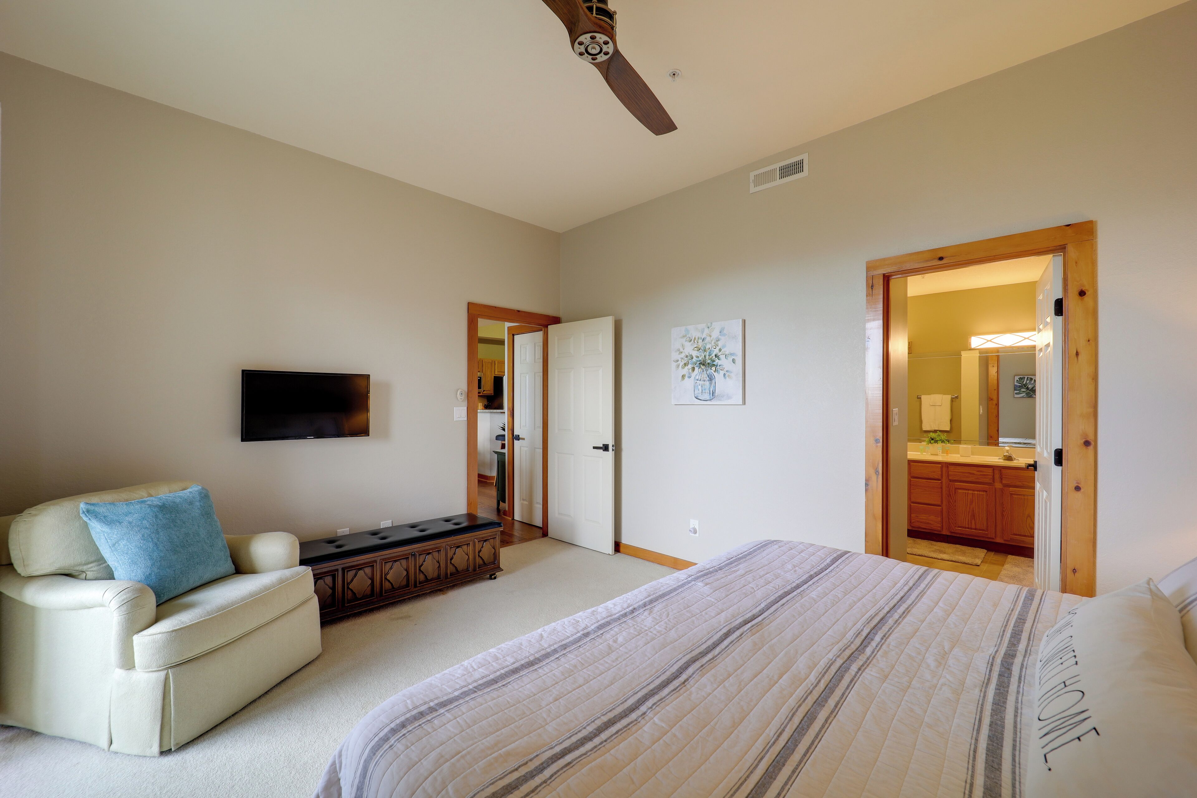 A bedroom with a large bed, a sofa, a TV, and a ceiling fan.