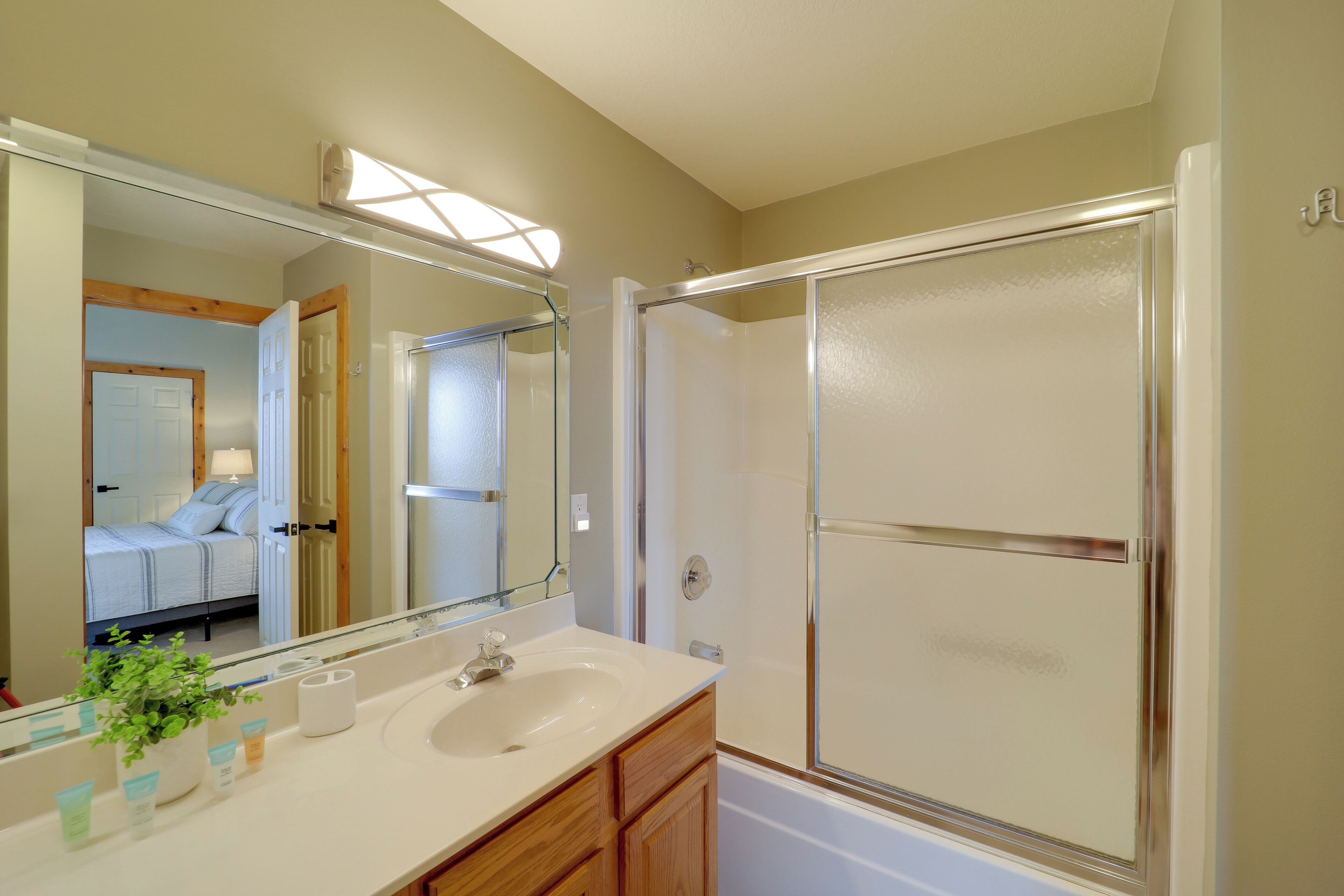 A bathroom with a large mirror, a sink, a shower, and a visible bedroom door.