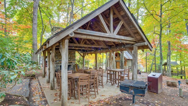 A rustic wooden pavilion with tables and chairs, surrounded by trees with autumn foliage.