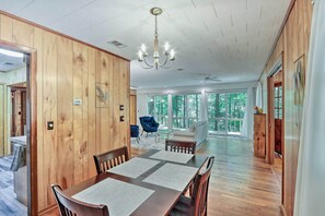 A spacious dining area with a wooden table and chairs, a chandelier, and large windows offering a view of the outdoors. - Secluded Franklin Cabin w/ Furnished Deck! (Franklin)
