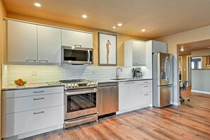 Una cocina moderna con electrodomésticos de acero inoxidable, armarios blancos y piso de madera.