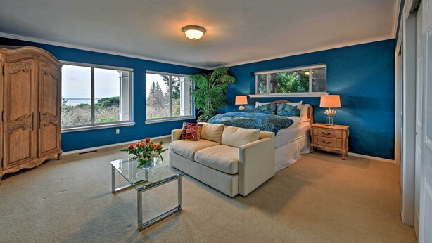 A bedroom with a large bed, a nightstand, a dresser, and a window with a view. - Airy Home Near Anacortes w/ San Juan de Fuca Views (Anacortes)