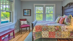 A bedroom with a large bed, a chair, a bench, and a window with a view of greenery. - Restored Mars Hill Home on 1 Acre: Walk to Town! (Mars Hill)