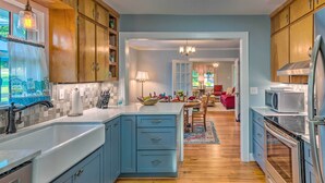 Una cocina moderna con armarios azules, encimera blanca y electrodomésticos de acero inoxidable. Cuenta con un rincón comedor con una silla roja y una araña.