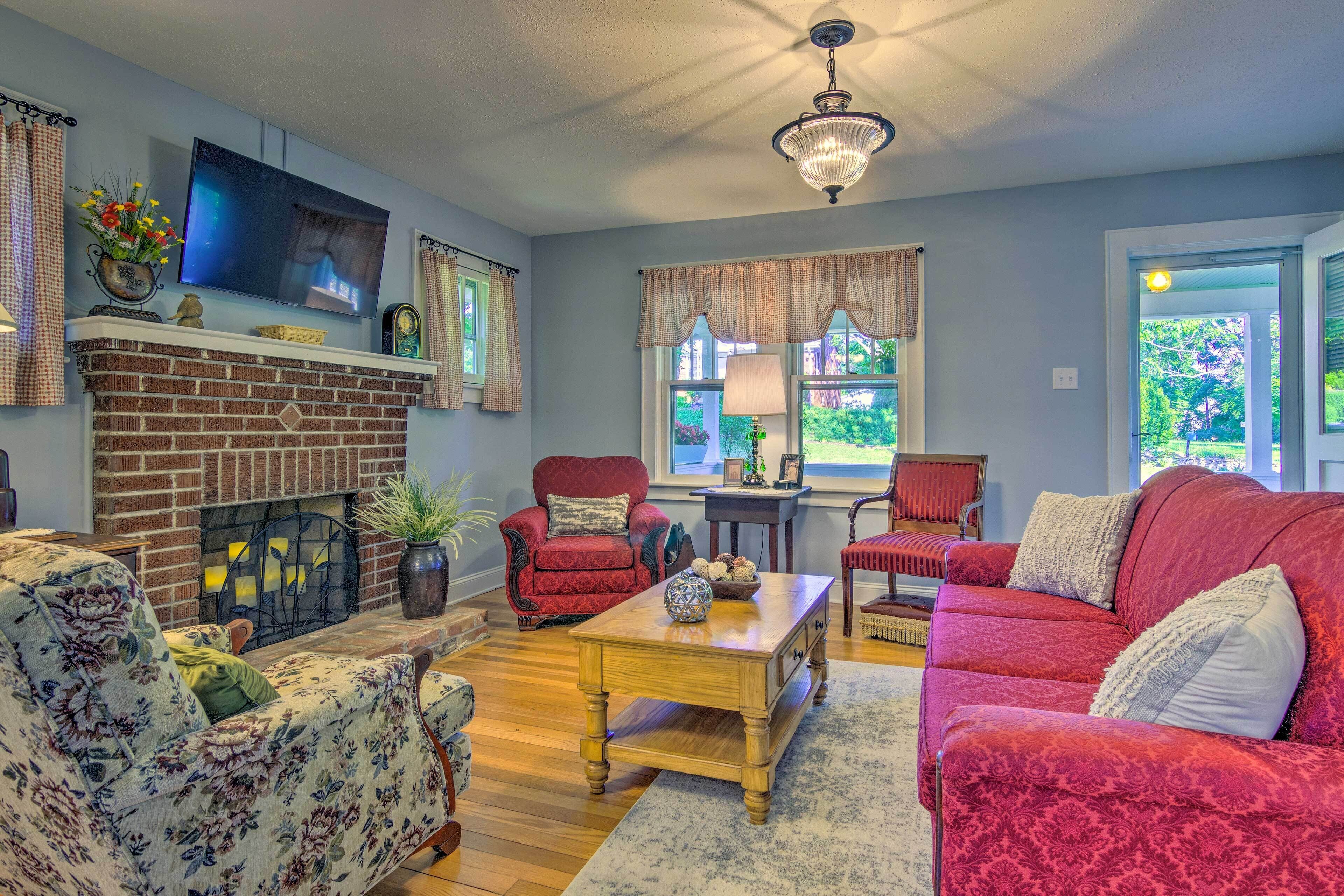 A living room with a brick fireplace, red armchairs, a wooden coffee table, and a television mounted on the wall.