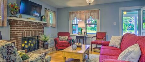 A living room with a brick fireplace, red armchairs, a wooden coffee table, and a television mounted on the wall.