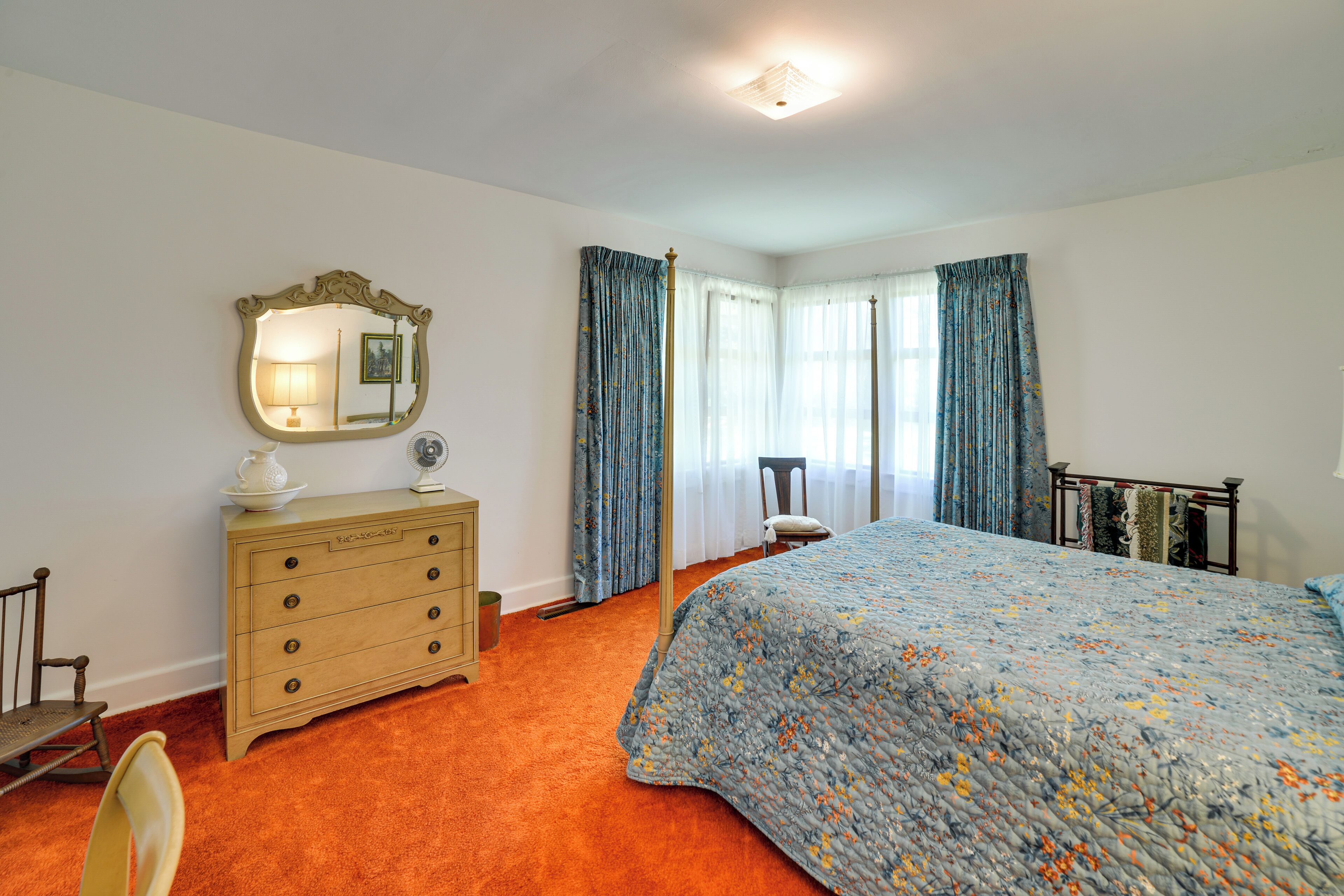 A bedroom with a large bed, a dresser, a chair, and a mirror.