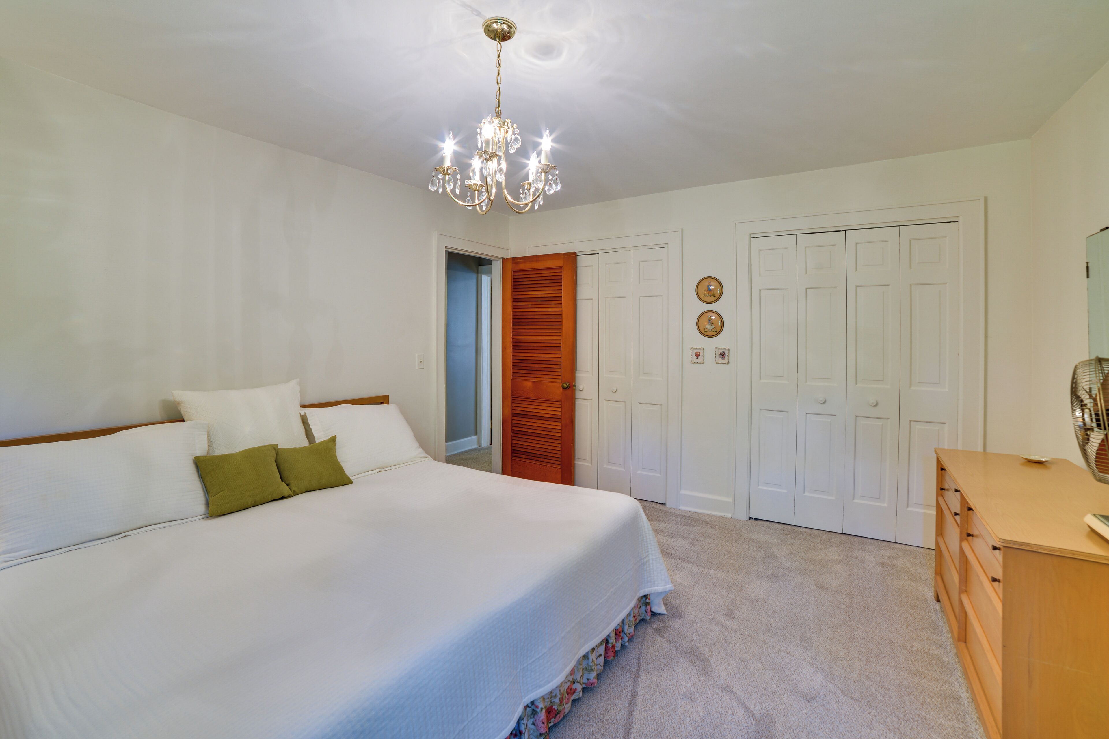 A bedroom with a large bed, a wooden door, a dresser, and a chandelier.