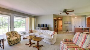 Ein Wohnzimmer mit einer Eckcouch, einem blumigen Sessel und einem Couchtisch. Im Hintergrund befinden sich ein Fernseher und ein Schrank.