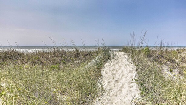 Ein sandiger Pfad führt zum Strand, umgeben von Gras.