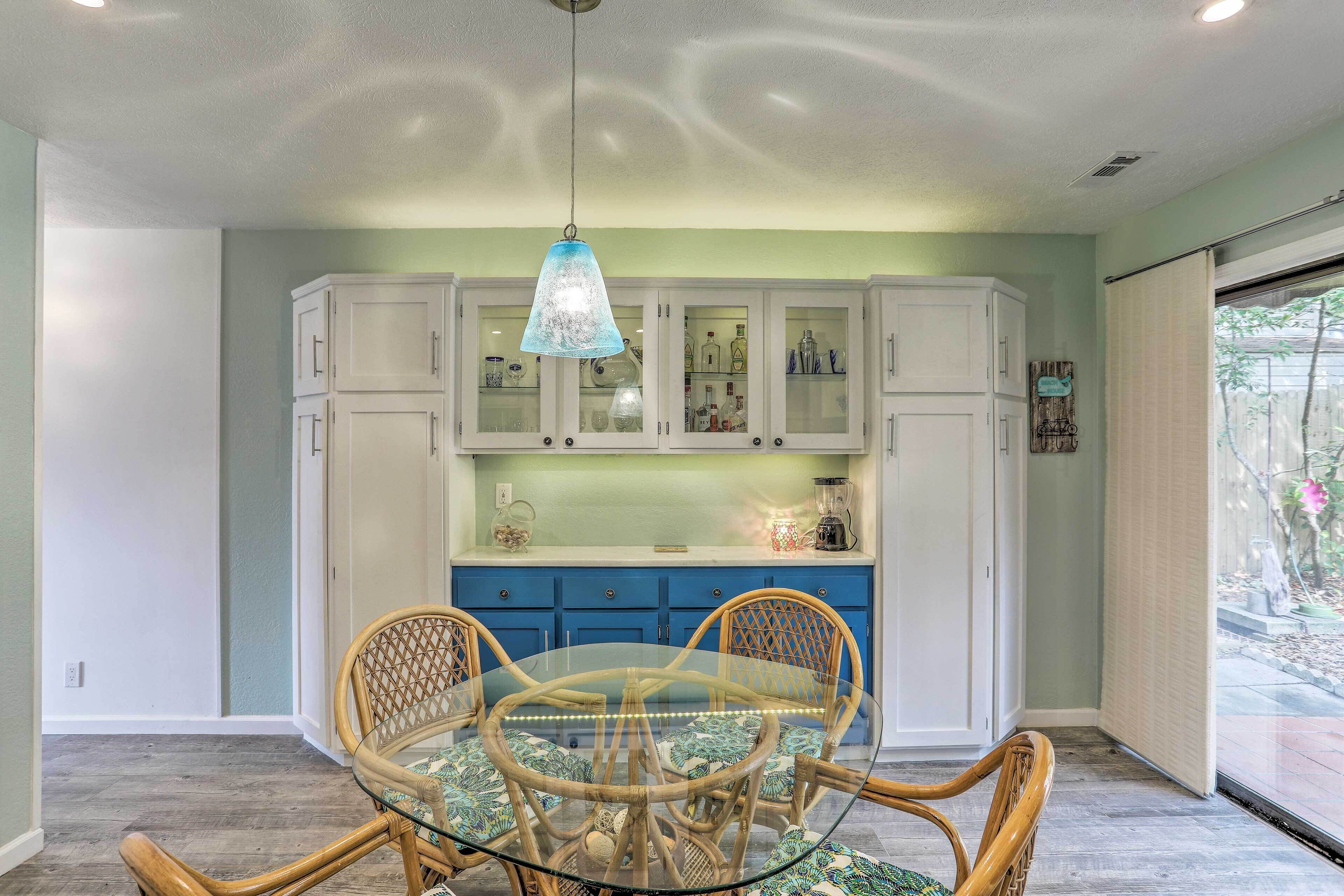 A dining area with a glass table surrounded by wicker chairs, white cabinets with glass doors, and a hanging light fixture.